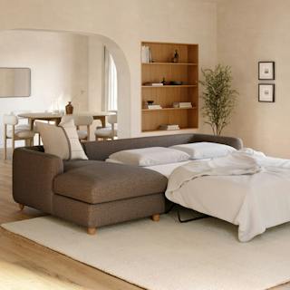 Brown sectional sleeper sofa with a chaise lounge and pull-out bed with white bedding in a neutral living room.