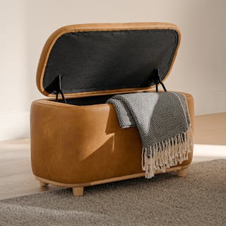 A leather storage ottoman with the lid open and a throw blanket draped over the side.