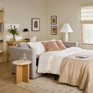Gray sleeper sofa with white bedding in a cozy, neutral living room.