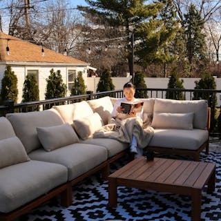 Person reading on the Cove 102.75" Outdoor Armless Modular Sectional in Basket Beige. Photo by @nomukaugc