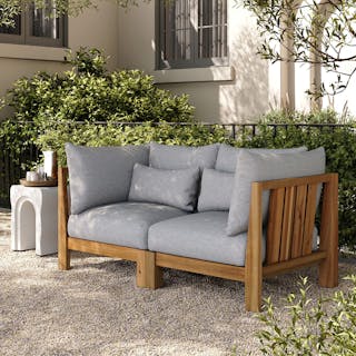 Sunny patio with greenery, featuring the Cove 68.5" Outdoor Modular Loveseat in Basket Gray