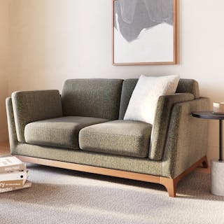 An ivory-colored bouclé loveseat with a patterned pillow on a wooden floor.
