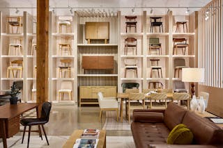 A furniture showroom scene featuring dining chairs arranged against a wall, with sofas, dining tables, and home office pieces styled in the foreground.