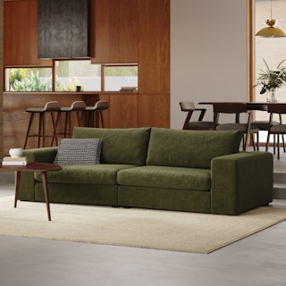 A green modular sofa in a modern living room with wooden walls and a dining set in the background.