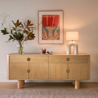 The Adel 71" Sideboard in White Oak, displaying floral arrangements, candles and table lighting