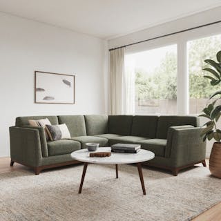 A green corner sectional sofa in a bright living room with a round woven coffee table.