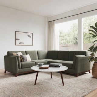 A green corner sectional sofa in a bright living room with a round woven coffee table.