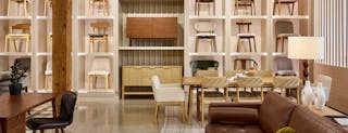 A furniture showroom scene featuring dining chairs arranged against a wall, with sofas, dining tables, and home office pieces styled in the foreground.