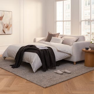 An ivory sofa bed with pillows and a throw blanket in a cozy living room.