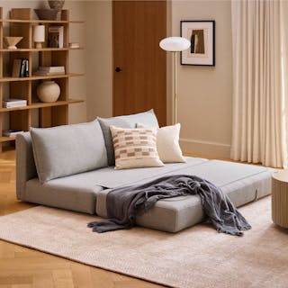 A grey sofa bed with pillows and a blanket in a cozy living room.