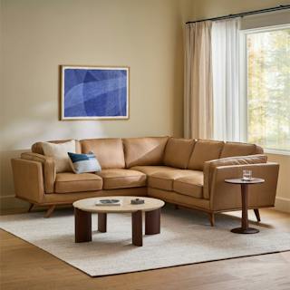 Timber corner sectional in Charme Tan leather with a wood base and accent pillows in a neutral mid-century modern living room.