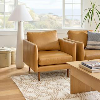 Two tan Bella Caramel leather Burrard Lounge Chairs with tapered walnut wood legs beside a white floor lamp in a bright coastal living room with ocean views.
