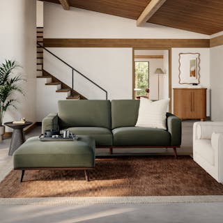 Green mid-century modern sofa with matching ottoman in a bright living room with a wood beam ceiling.