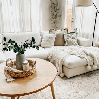 White Beta sectional sofa with a chaise, textured accent pillows, and a cream knit throw beside a round wood coffee table.