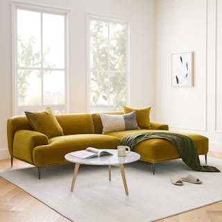A yellow velvet sectional sofa with a right chaise in a bright living room with two large windows.