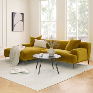 A yellow velvet sectional sofa in a bright living room with large windows.